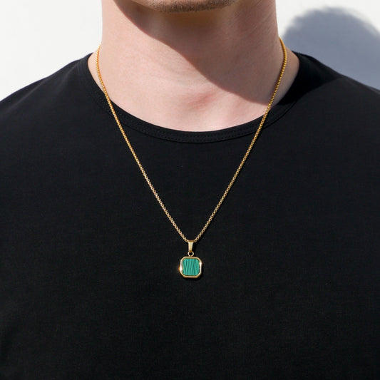 Gold chain necklace with small green square pendant on black crewneck shirt