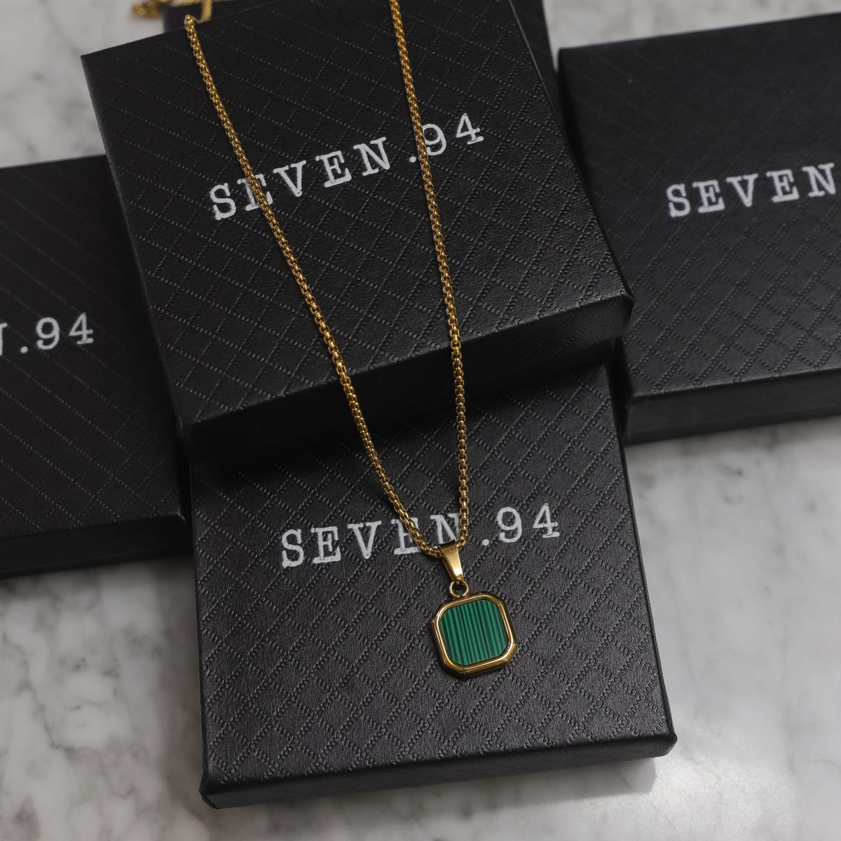 Gold chain necklace with green square pendant, shown with SEVEN.94 gift boxes