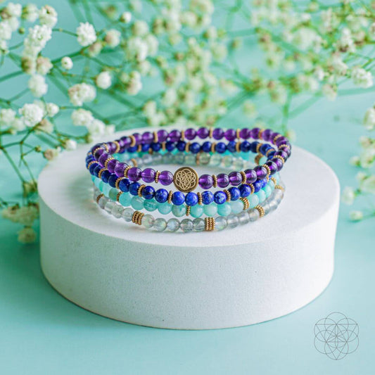 Set of 4 beaded gemstone bracelets in purple, blue, and clear stones with gold charm