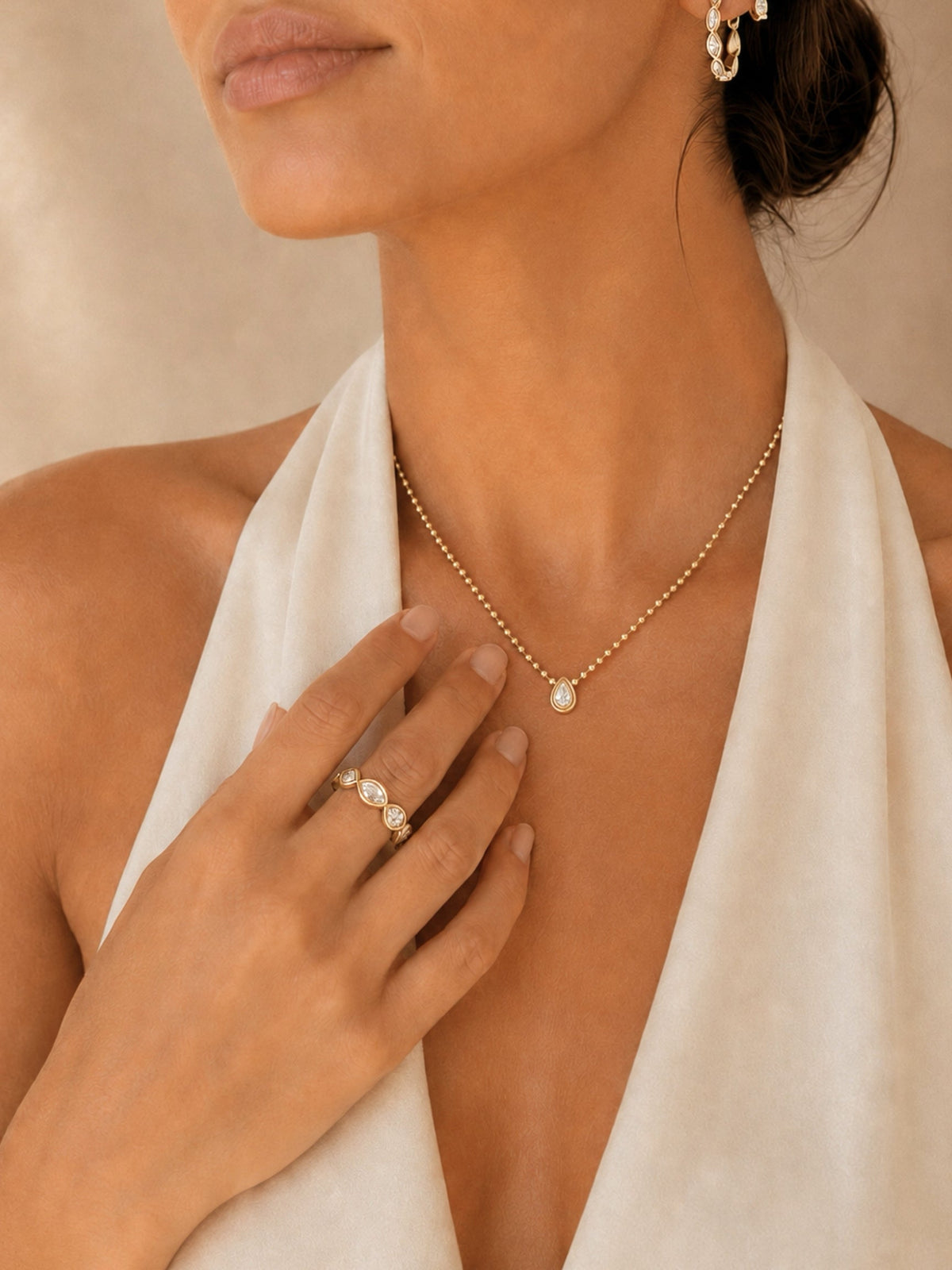 Gold teardrop pendant necklace, shown with ring and hand near collarbone