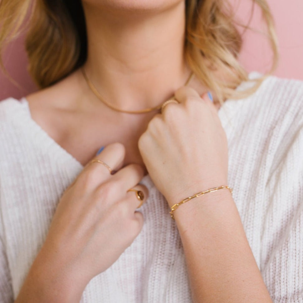 Gold-filled paperclip bracelet worn with a gold necklace and rings.