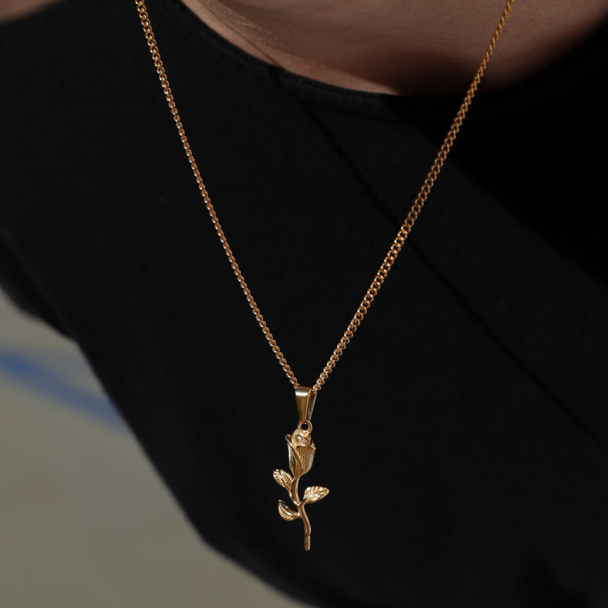 Gold rope chain necklace with rose pendant and leaf charm, close view
