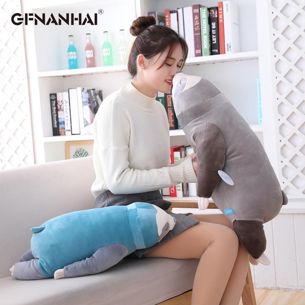 Grey sleeping sloth plush with closed-eye face, held upright beside a couch