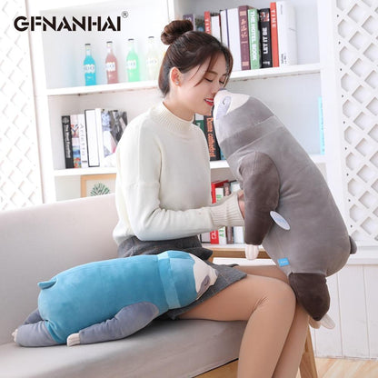 Grey sleeping sloth plush with closed-eye face, held upright beside a couch