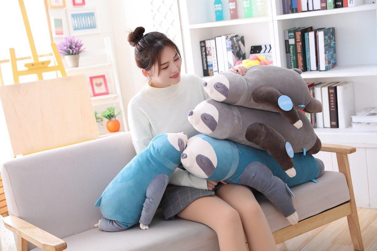 Blue and grey sleeping sloth plush, lying across a person’s lap