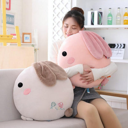 Plush rabbit pillow in pink with long ears and stitched face; paired with grey pillow.