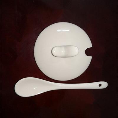 White ceramic mug lid with face-like panel and matching spoon accessory