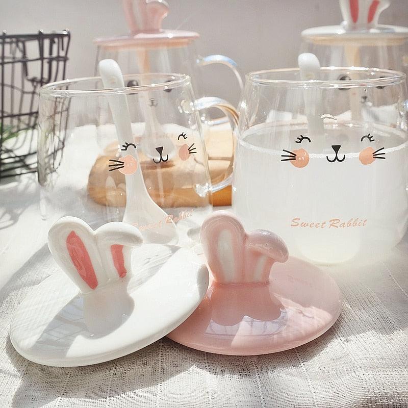 Two glass bunny mugs with bunny-ear lids, bunny face print, and matching spoon rest