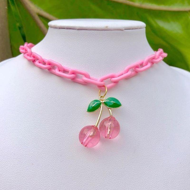 Pink chain necklace with three cherry charms, green leaf accents, and gold-tone link