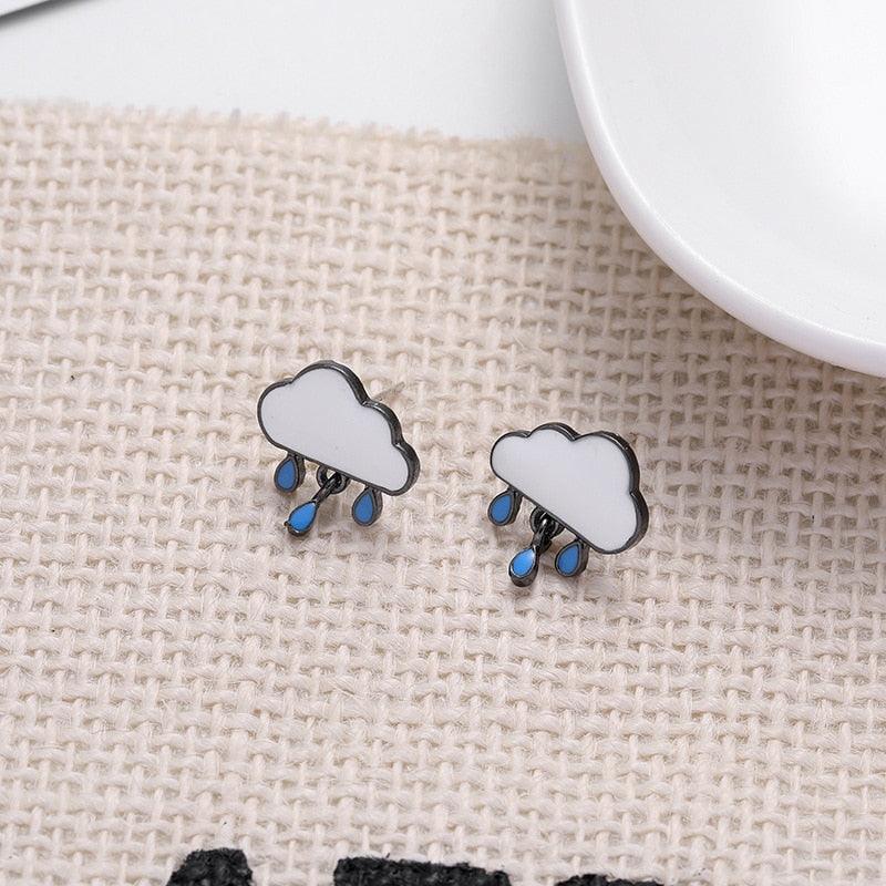 Cloud-shaped stud earrings with blue raindrops, shown on textured fabric