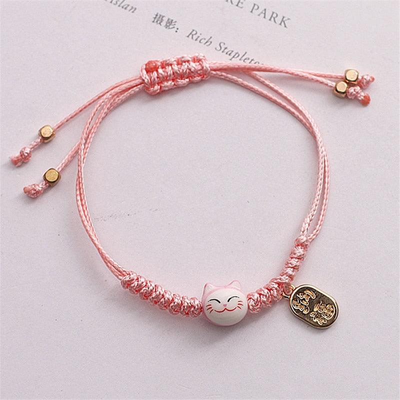 Pink cat charm bracelet with braided cord, light pink cat bead, and gold-tone tag