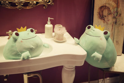 Two green frog plush toys with yellow crowns, sitting on tabletop