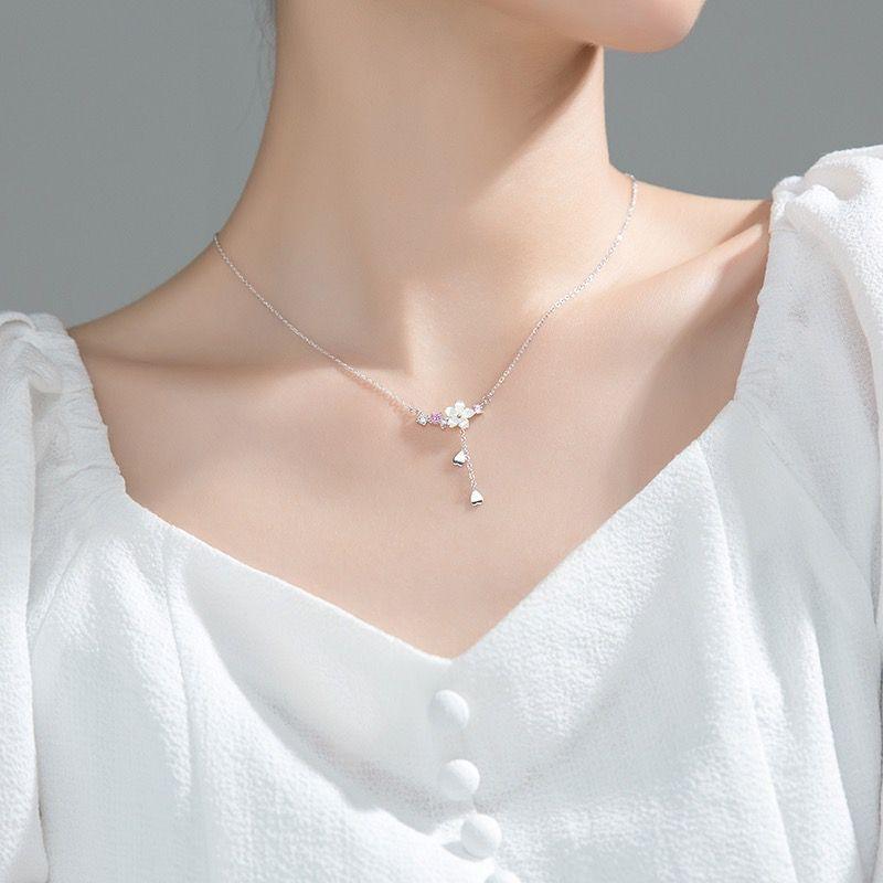 Silver-tone sakura pendant necklace worn on neckline, with flower charm and pink stones