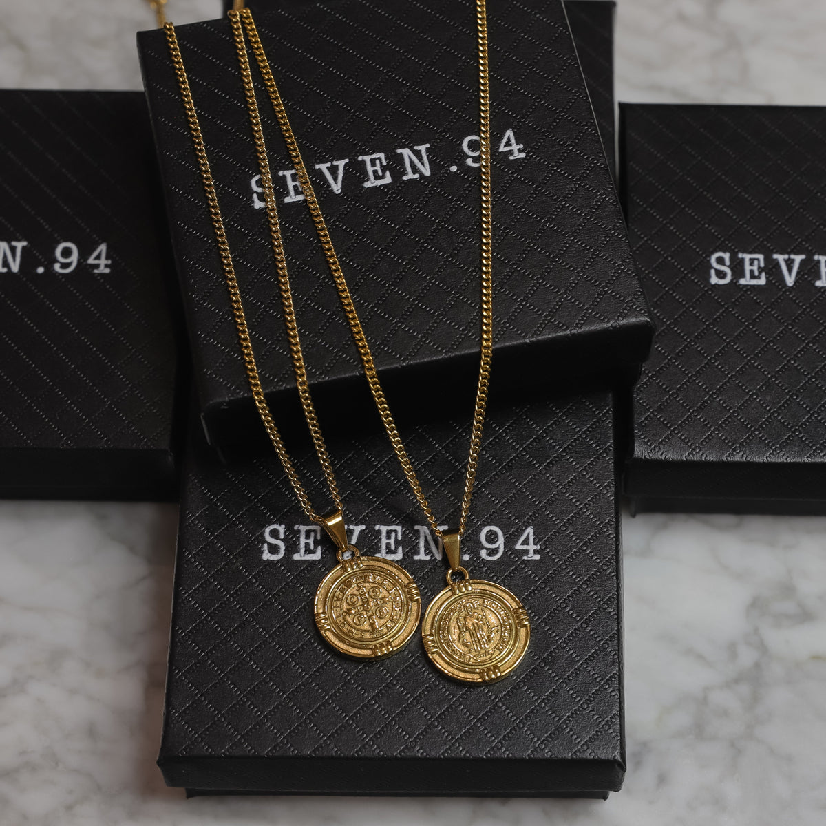 Gold Saint Benedict medal necklaces displayed with round pendants on gift bags
