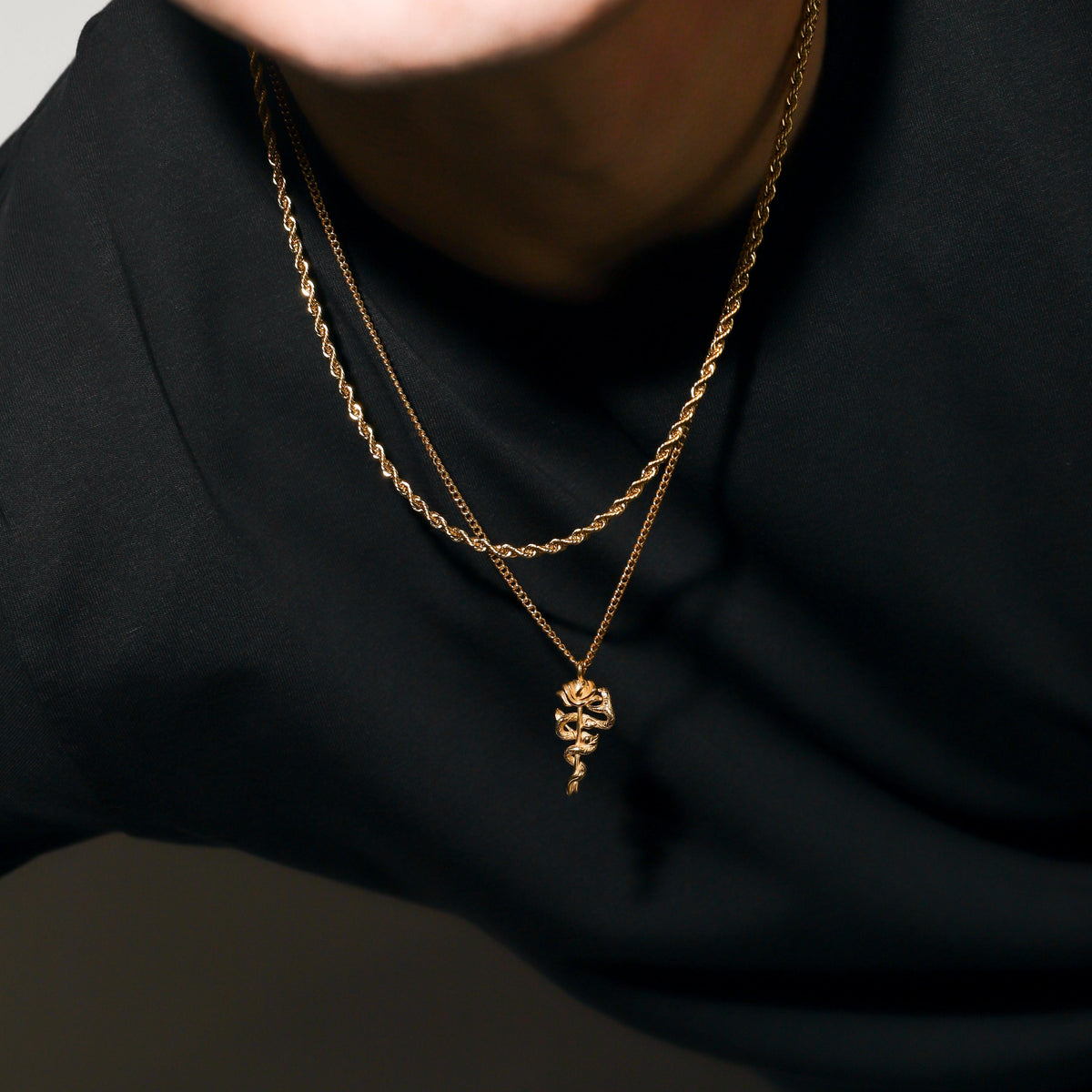 Gold serpent rose pendant necklace with coiled rose charm on a black crewneck