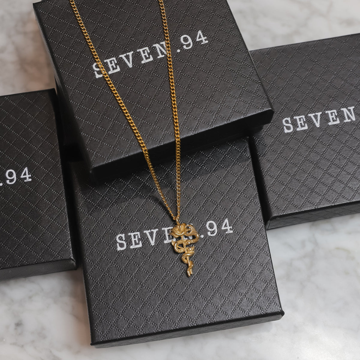Gold serpent rose pendant necklace with coiled rose charm resting on gift boxes