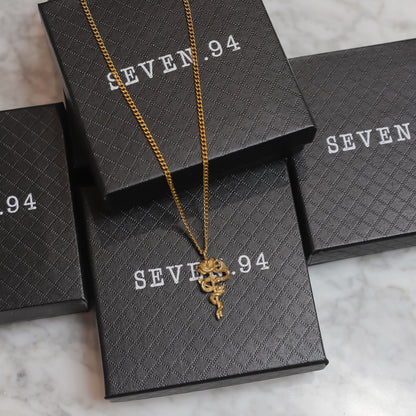 Gold serpent rose pendant necklace with coiled rose charm resting on gift boxes