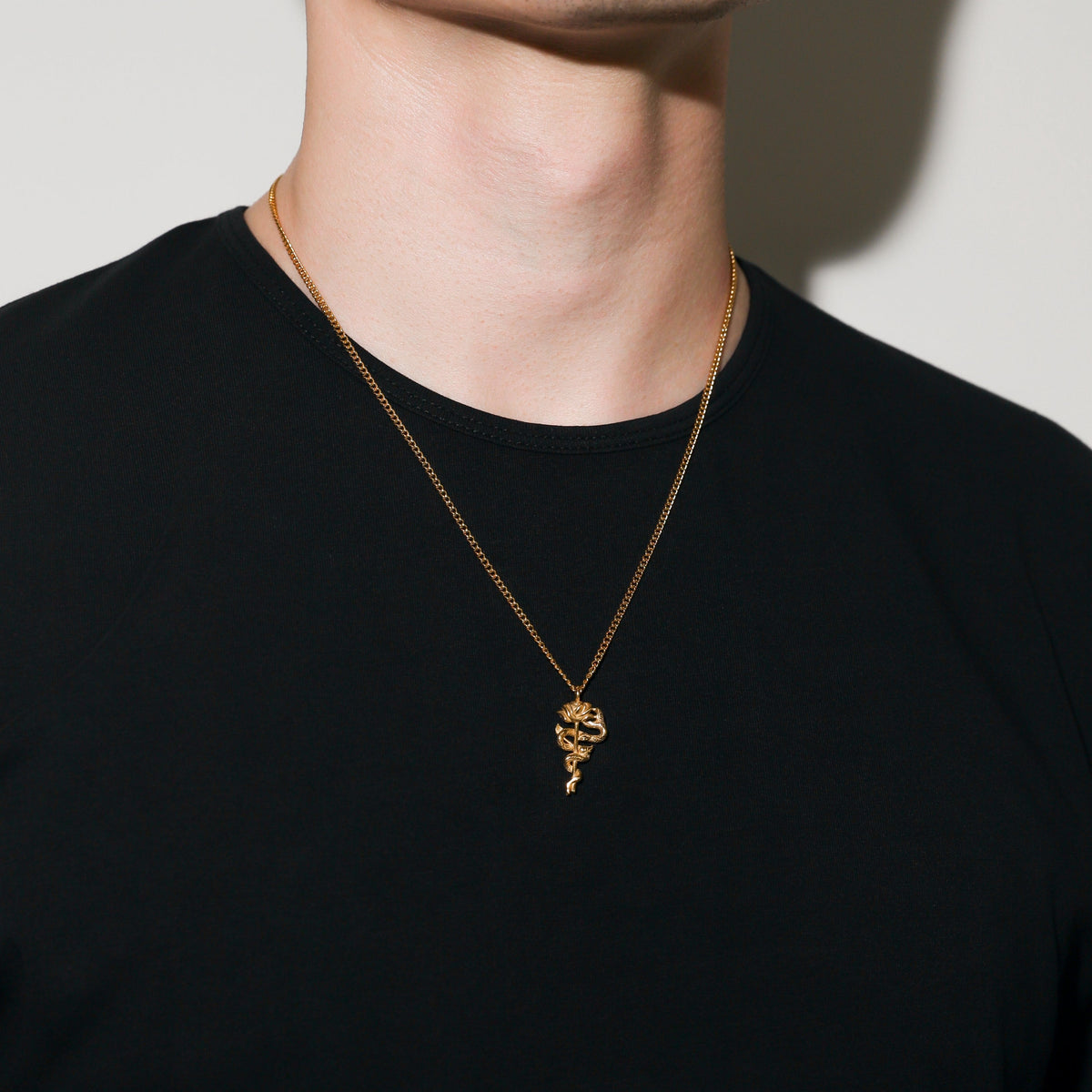 Gold serpent rose pendant necklace featuring a small coiled rose charm at the collar