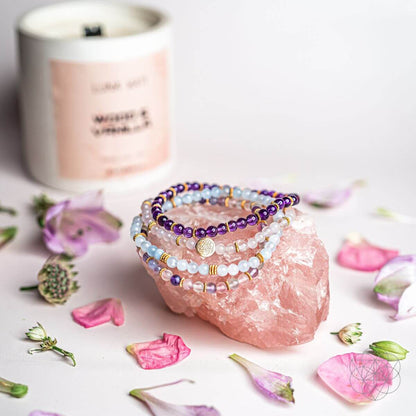 Gemstone bracelet stack with purple, white, and pale blue beads beside a pink crystal
