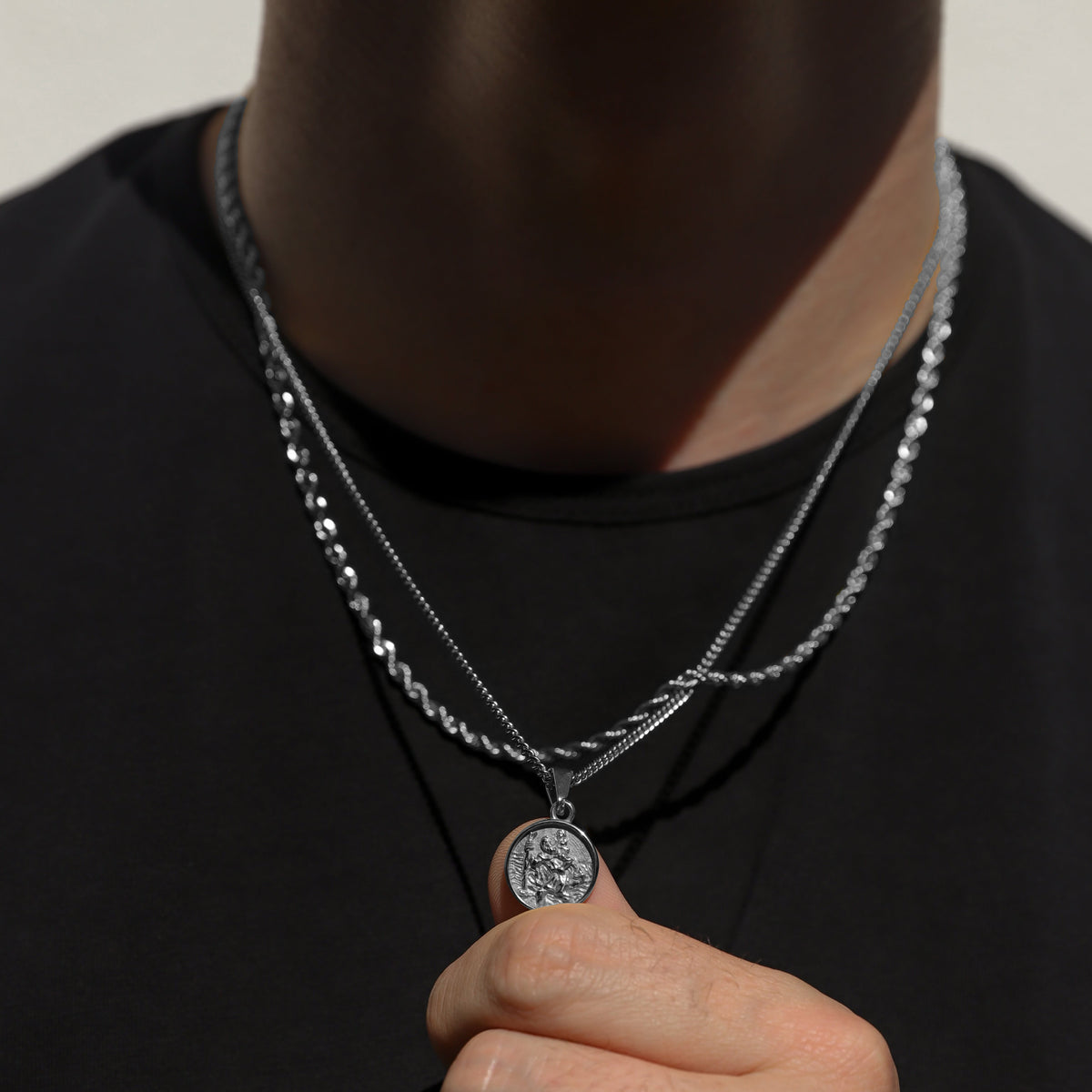 Silver rope necklace set with Saint Christopher pendant, held near the collar