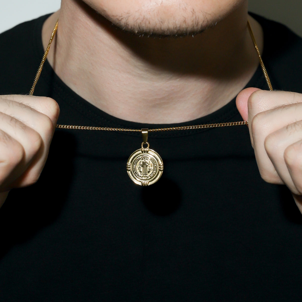 Gold Saint Benedict medal necklace clasp and round medal pendant held near collar