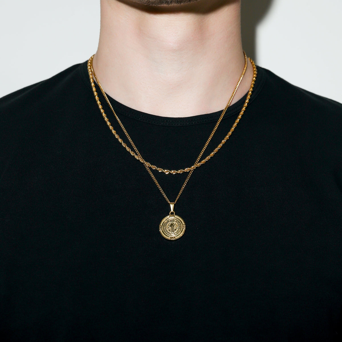 Gold Saint Benedict medal necklace with round medal pendant on black shirt