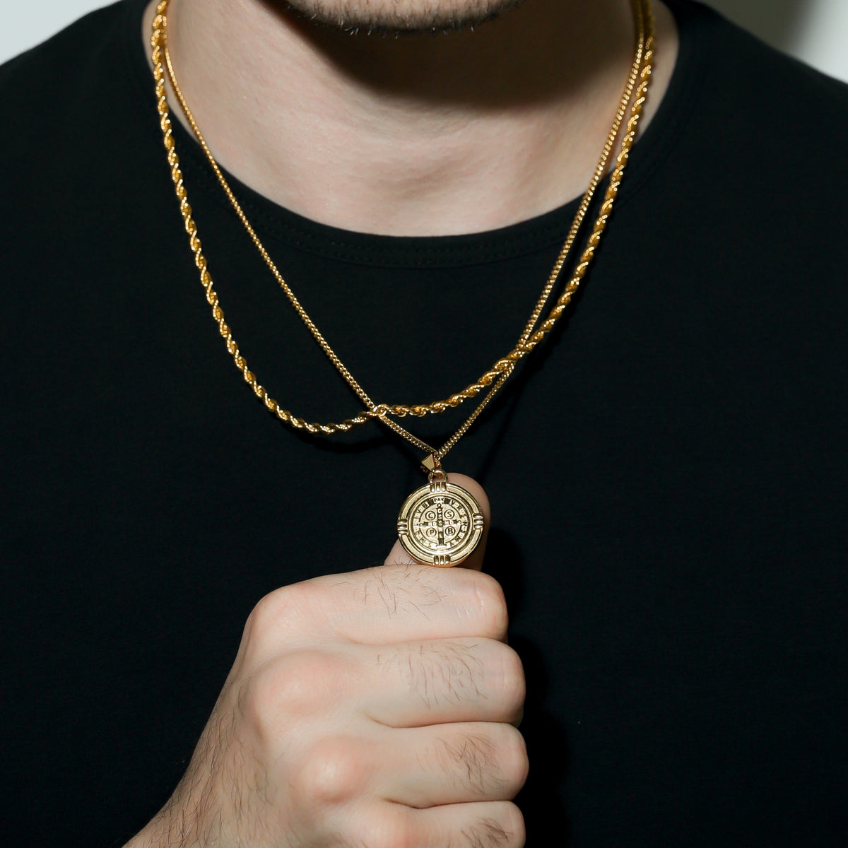 Gold Saint Benedict medal necklace close-up, round medal pendant held at neckline