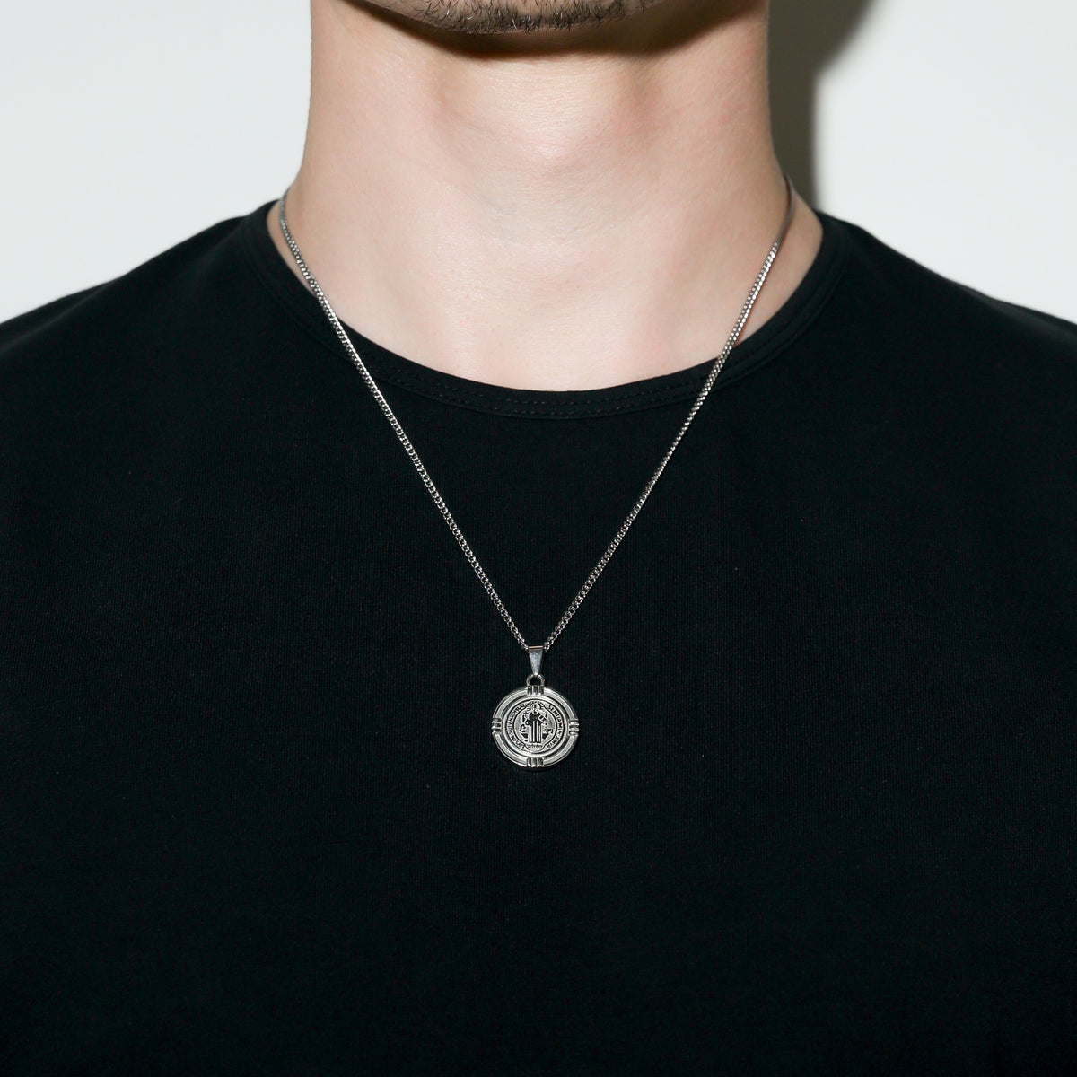 Silver Saint Benedict medal necklace on a man’s neck with round medal pendant