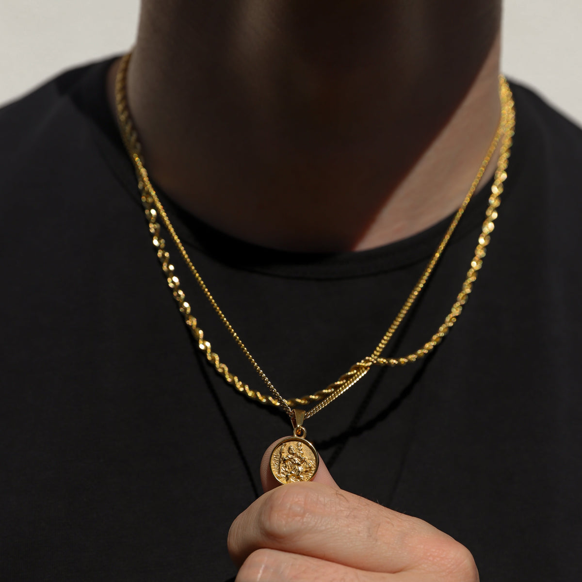 Gold rope necklace set with Saint Christopher pendant, pendant held near collar