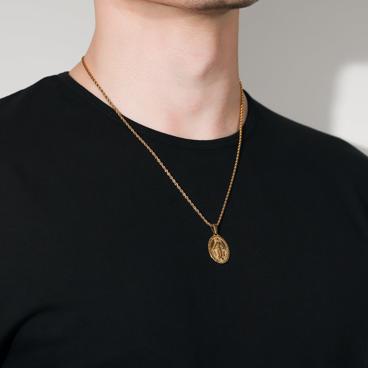 Gold Saint Mary pendant necklace layered look on black shirt, oval charm