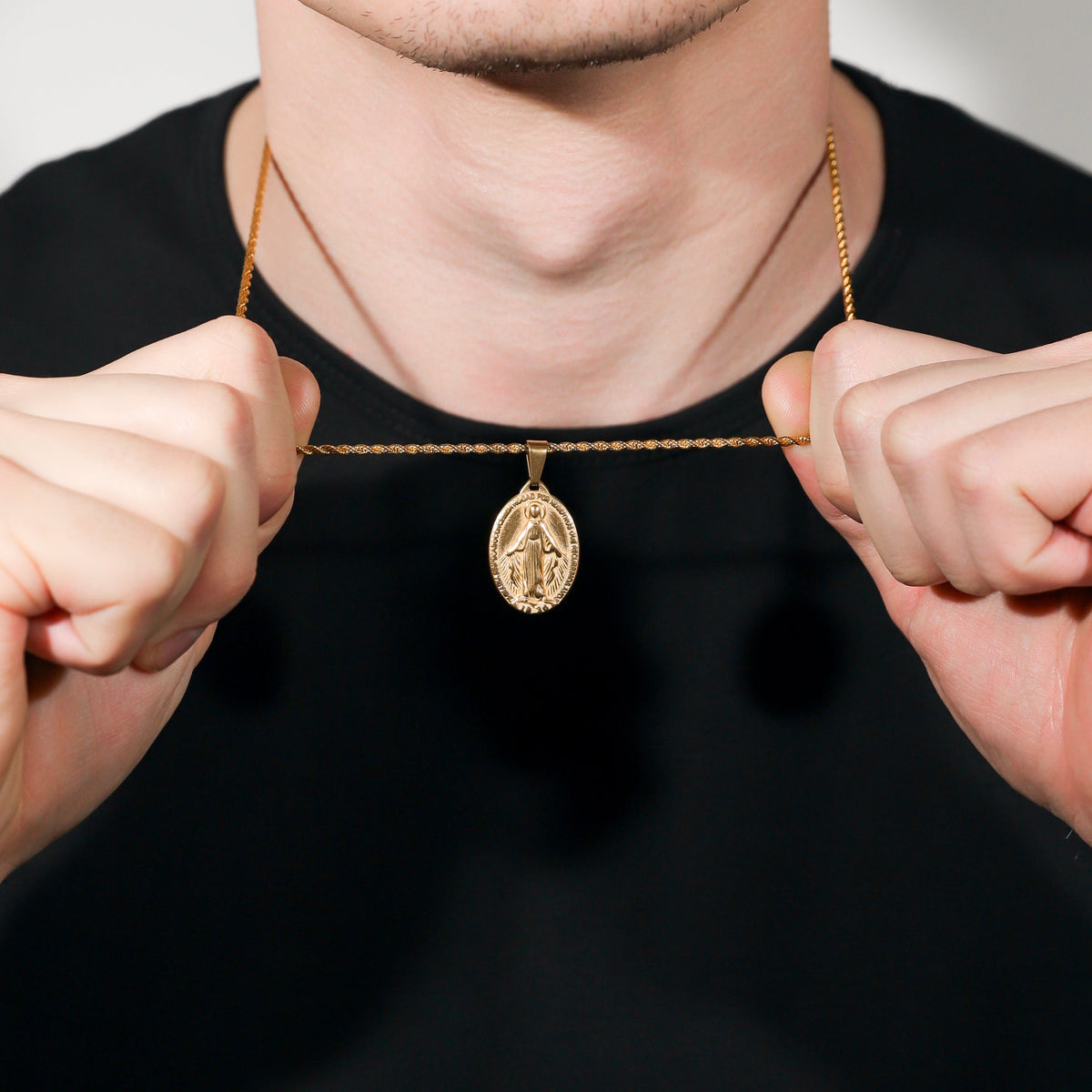 Gold Saint Mary pendant necklace close-up, hands holding chain at collar