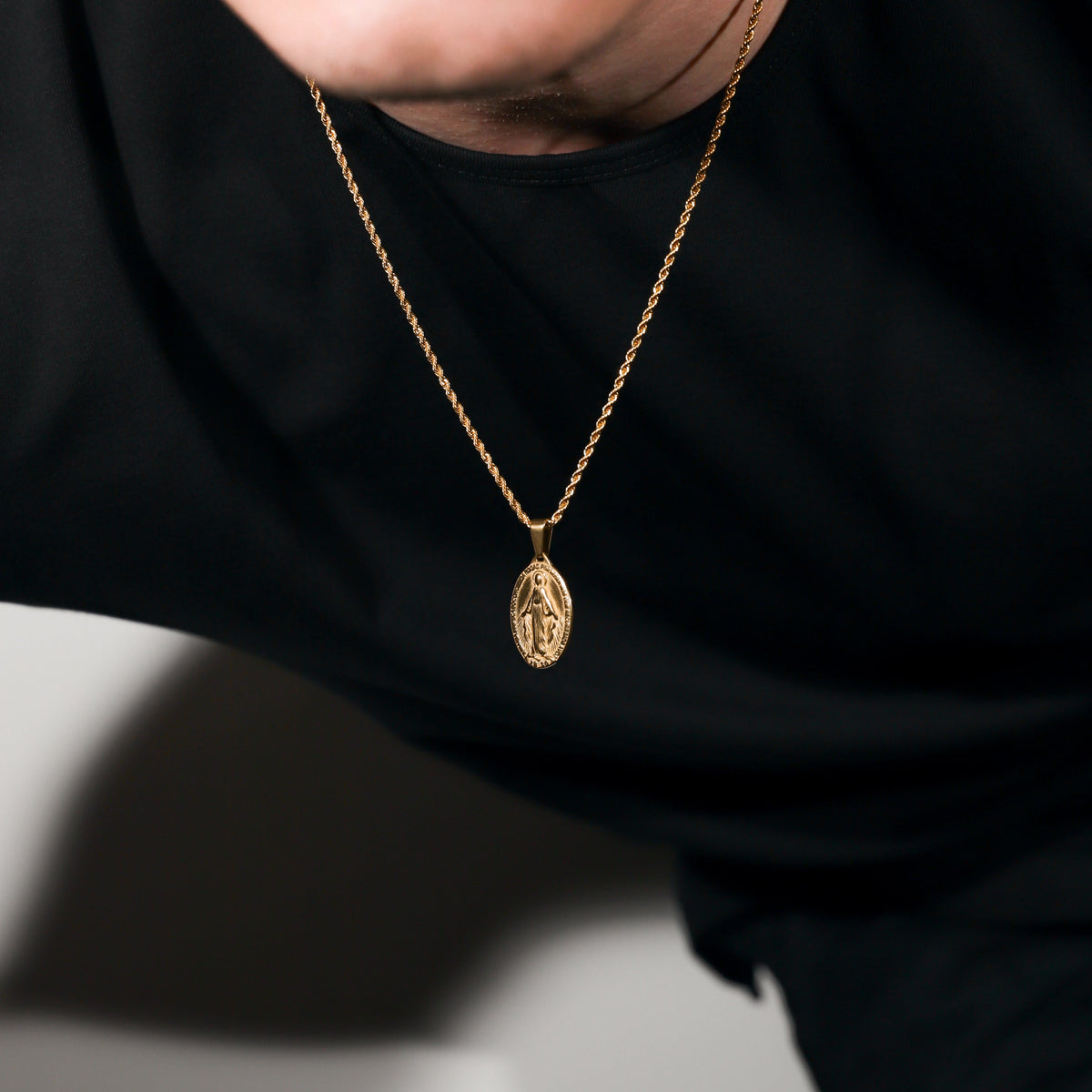 Gold Saint Mary pendant necklace on black shirt, oval charm on chain