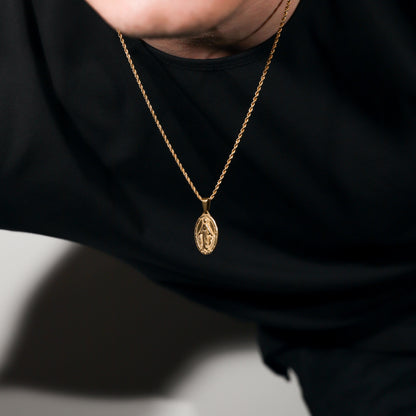 Gold Saint Mary pendant necklace on black shirt, oval charm on chain