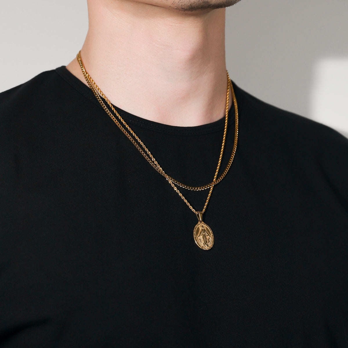Gold Saint Mary pendant necklace on black shirt, oval pendant on chain