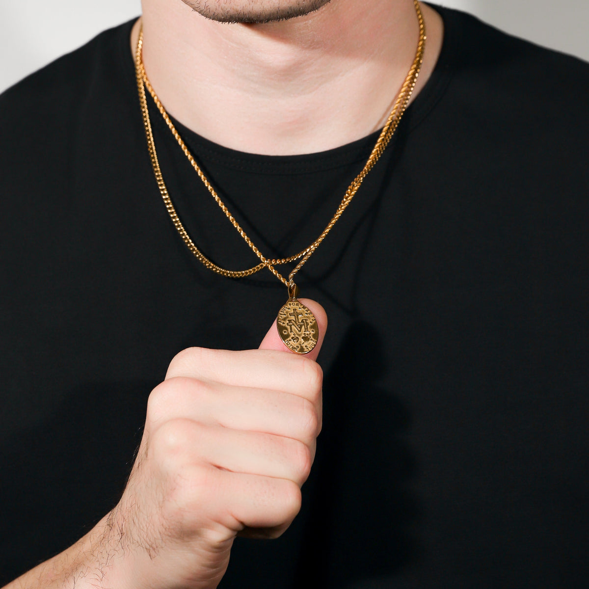 Gold Saint Mary pendant necklace held near chest, oval medallion pendant