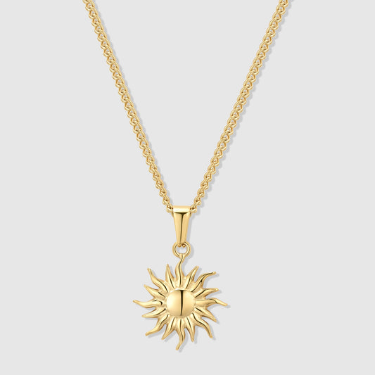 Gold sun pendant necklace with small starburst charm on a curb chain.