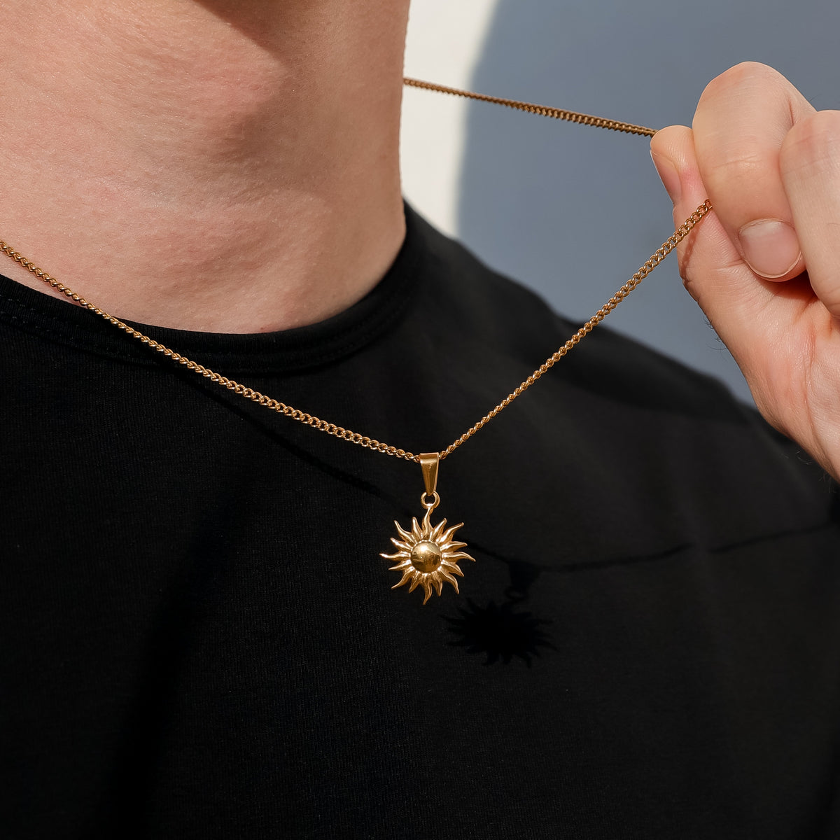 Gold sun pendant necklace close-up near clasp; sunburst charm on chain.