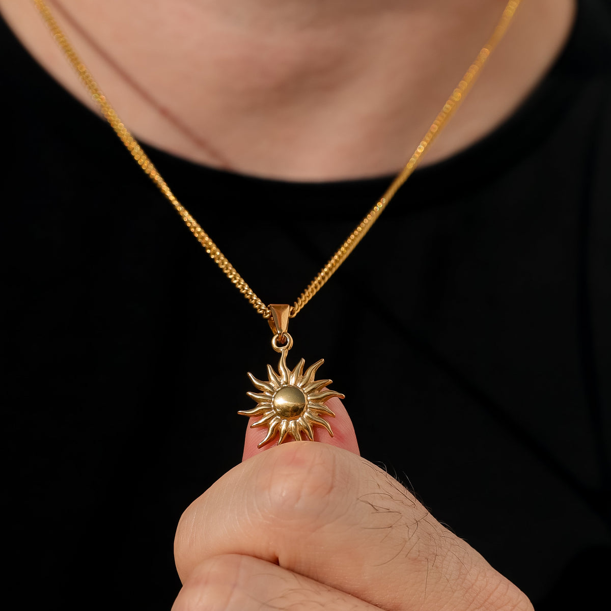 Gold sun pendant necklace held in hand; starburst charm with circular center.