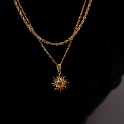 Gold sun pendant necklace with starburst charm hanging from chain.