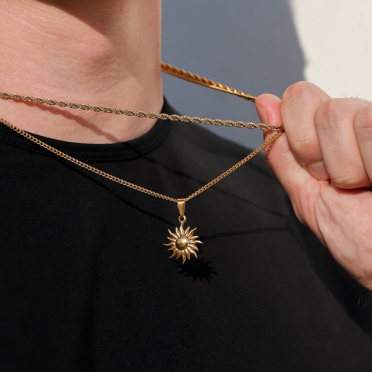 Gold sun pendant necklace close-up of chain and sun charm held by hand.