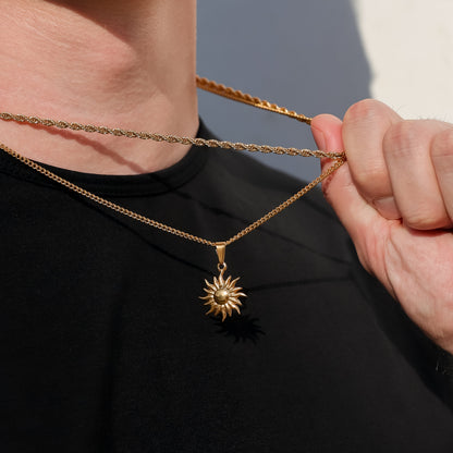 Gold sun pendant necklace close-up of chain and sun charm held by hand.