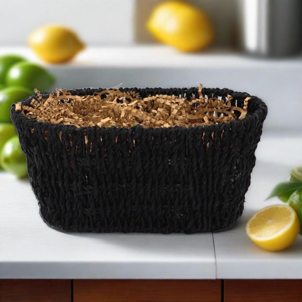 Black woven gift basket with open top and shredded filler on a white table.