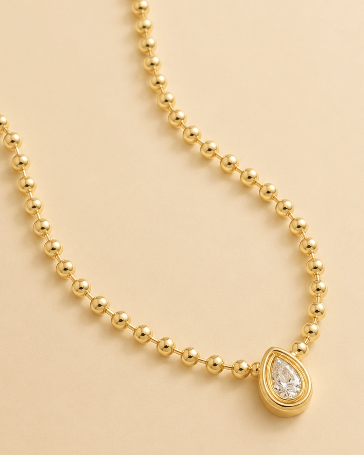Gold ball-link chain with bezel-set round stone and teardrop diamond-style drop