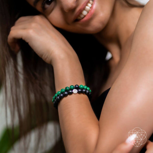 Two beaded bracelets on wrist: matte black beads and green stone beads