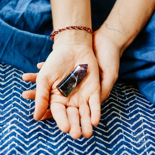 Small faceted cleansing crystal shard held in open hands over blue fabric