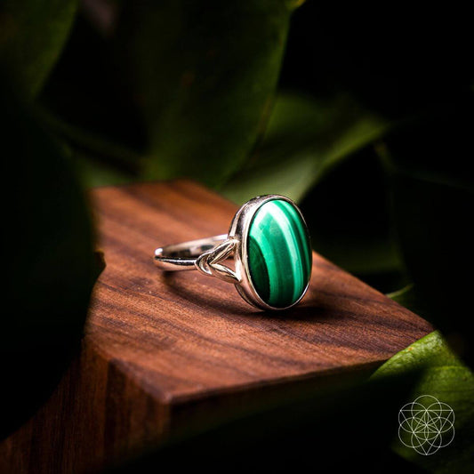 Silver ring with oval green gemstone bezel setting, decorative shoulders visible