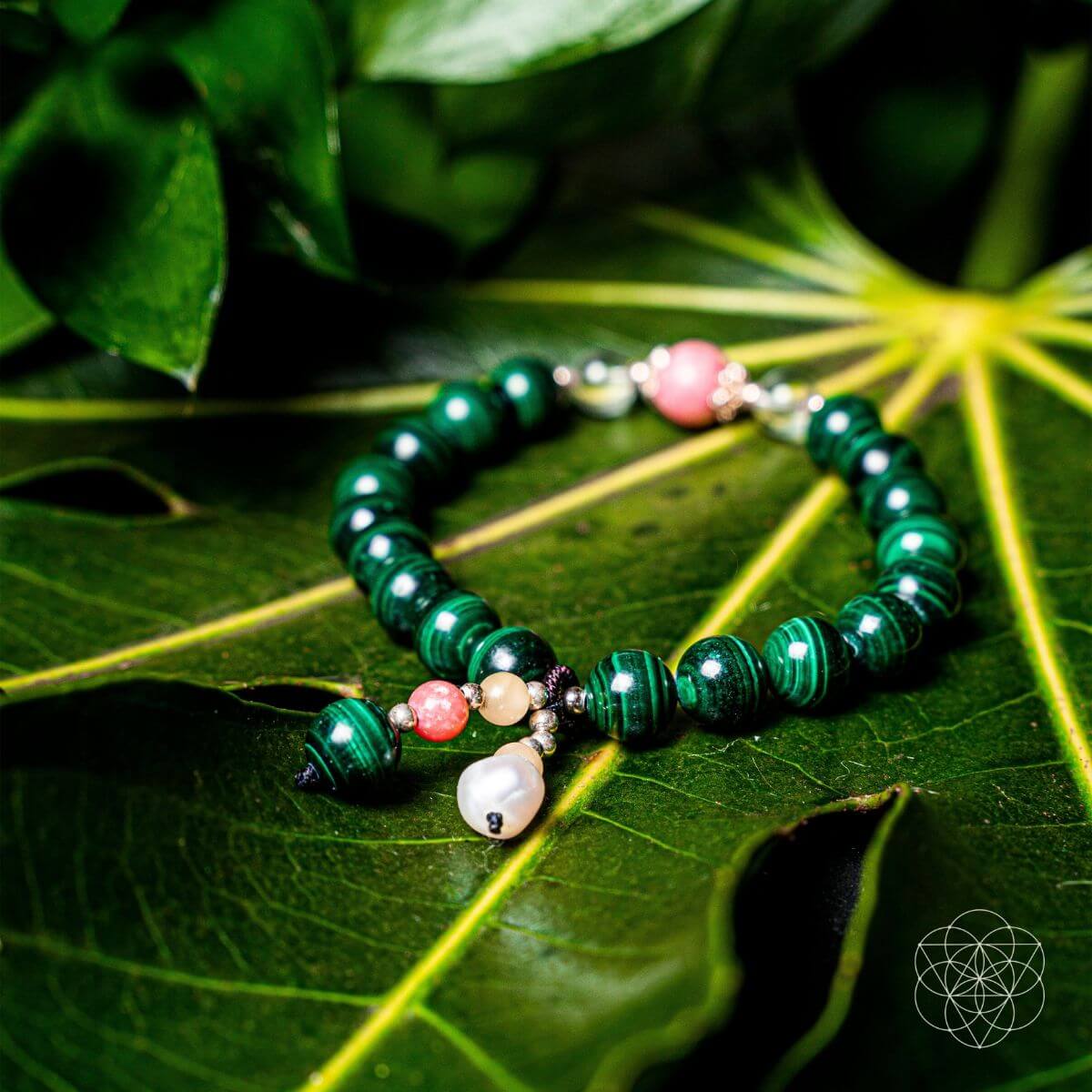 Close-up gemstone bracelet with glossy green beads and pearl-like dangling charm