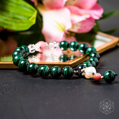 Laid flat bracelet with green round beads, pearl-like center, and pink-and-gold charms