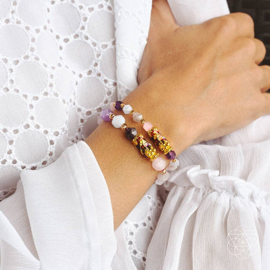 Gemstone beaded bracelet with gold Pixiu charm on wrist, purple and pale pink beads