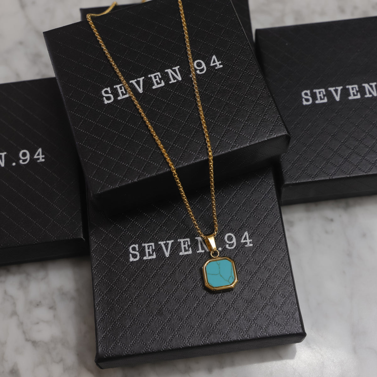 Gold-tone chain necklace with turquoise square stone pendant on product boxes